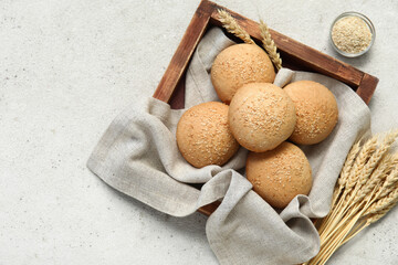 Wooden board of fresh buns with sesame seeds and wheat on white background