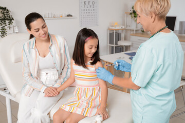 Obraz premium Female pediatrician vaccinating little girl and mother in clinic