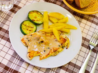 Chicken breast with white sauce with pepper, served with side dish of French fries and fried piece of zucchini. Hearty dish of poultry meat and vegetables