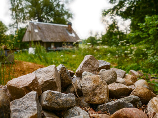 A pile of rocks in focus, small old country barn or storage in the background. Selective focus gives rustic and cozy appearance. Rural area theme. Old construction material.