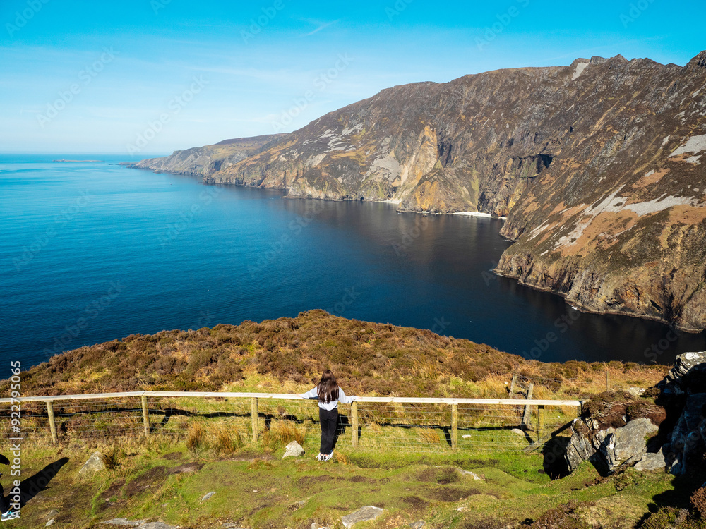 Wall mural Young teenager girl explore beautiful nature scenes of Sliabh Liag viewing platform. Famous landmark in Ireland. Warm sunny day. Irish nature landscape. Travel and tourism industry.