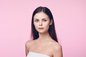 Beautiful young woman with long brown hair posing on a pink background, with copy space