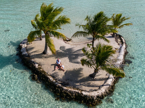 Aerial view from drone of a happy couple together on a small tropical island. The romantic vacation is on a heart shaped motu. - Powered by Adobe