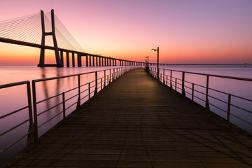 Pier. Path to the river. Dawn on the river with a large cable-stayed bridge. Vasco da Gama Bridge...