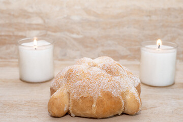 Delicious pan de muerto, behind it, two white candles. Amate paper background. Mexican tradition about death.