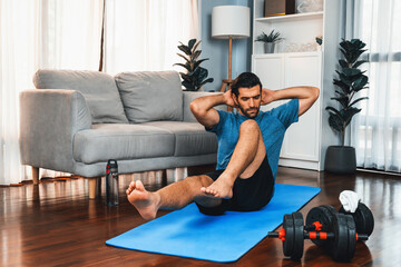 Athletic and sporty man doing crunch on fitness mat during home body workout exercise session for fit physique and healthy sport lifestyle at home. Gaiety home exercise workout training concept.