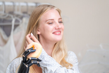 A young woman is using a robotic prosthetic arm attached to her body. She controls her hand to pick...