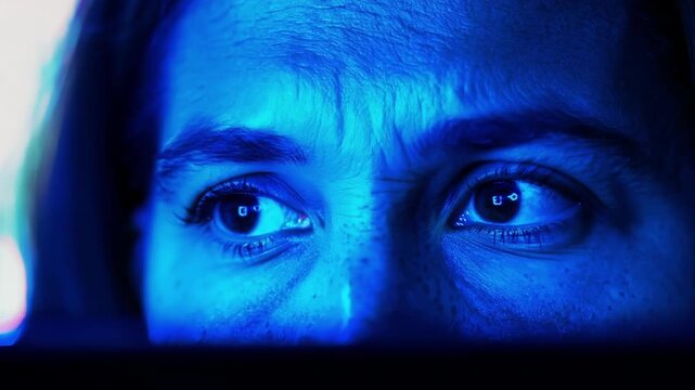 An intense closeup of a protesters face illuminated by the blue light of their laptop screen as they join a virtual protest or online rally.