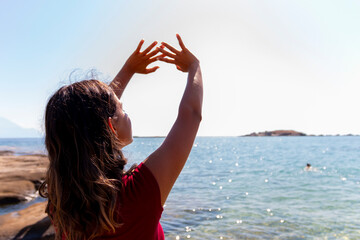 A young woman looks at the sun and uses her hands to make a shadow over her eyes, showing enjoyment.