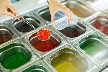 Hands of vendor preparing bubble tea, scooping red pearls from stainless steel container into...