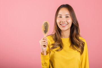 Portrait of Asian beautiful young woman smile combing her hair, happy female long healthy hair holding with hairbrush comb, studio shot isolated on pink background