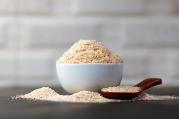 Psyllium Husk (Isabgol) in a ceramic bowl with a wooden spoon on a grey background