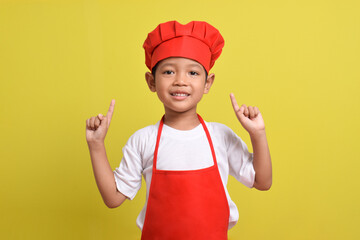 Cute little chef showing Blank Space above with hand gesture up isolated on yellow background. Asian boy wearing red apron and hat. Offer concept. Advertising banner