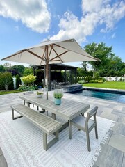 High-end outdoor living space, a backyard patio with pergola, outdoor rug,  tequila bar, dining set, couch, television, pool with waterfall, umbrella, fire pit and stunning grey patio. Modern vibe.