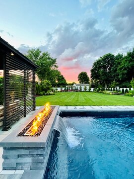 Stunning poolside gas fire pit filled with black glass compliments the in-ground, built in  pool at sunset. Provides the perfect amount of warmth for entertaining and can be enjoyed all year round. 