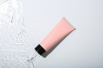 Cosmetic product. Tube with cream in water on light background, top view