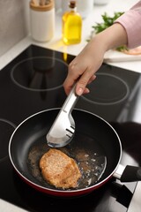 Woman cooking schnitzel in frying pan on stove, closeup