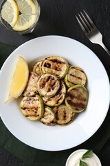 Tasty grilled zucchini slices served on black textured table, flat lay
