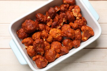 Baked cauliflower buffalo wings in baking dish on wooden table, top view