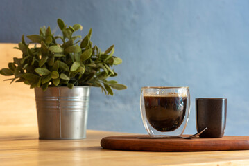 Hot black coffee cup on Wood office desk plant pot decor table blue background. Cup of Black Tea Green potted plant on office wooden desk springtime garden. freshness Home workplace decorate table
