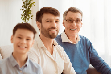 Multi-Generational Family. Joyful Senior Man, His Adult Son And Grandson Boy Smiling At Camera Sitting On Sofa At Home.