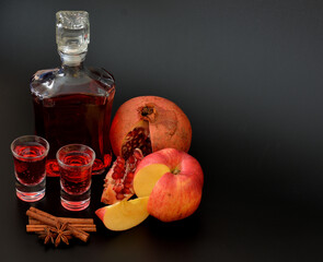 Apple pomegranate liqueur with cinnamon, anise and pieces of fruit on a black background, strong homemade alcohol in a bottle and two glasses.