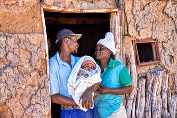 african village, happy mother ,father and baby, standing in front of the mud shack house, poverty