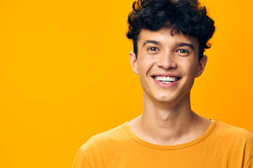 Cheerful young man with curly hair smiling against a bright yellow background, conveying joy and positivity through his expression and demeanor Perfect for lifestyle and happiness themes