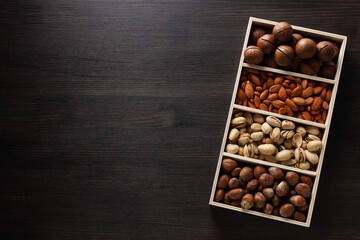 Wooden box with different nuts on a dark background
