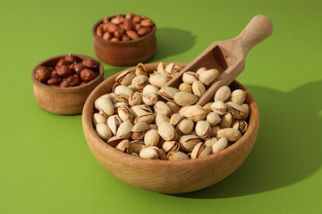 Different types of nuts in wooden bowls on a green background