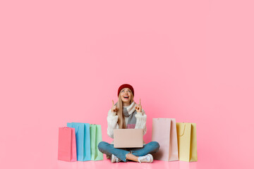 Excited pretty girl in winter clothes with laptop looking up at empty space, shopping online over yellow background