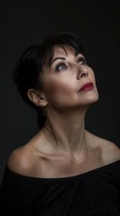 A woman with an elegant appearance looks thoughtfully upward in a dimly lit environment
