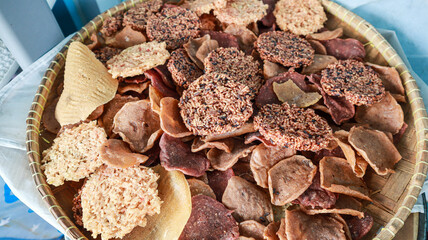 A variety of crispy snacks arranged in a woven bamboo tray, showcasing a colorful and textured assortment of snacks. Assorted Crispy Snacks in a Bamboo Tray Background.