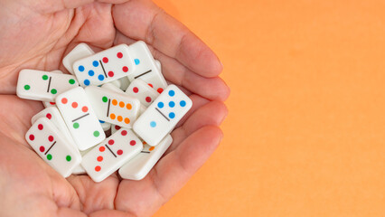 Close-up of hands holding colorful dominoes on an orange background Ideal for creative projects featuring childhood, board games, leisure activities, family playtime, and playful and colorful designs