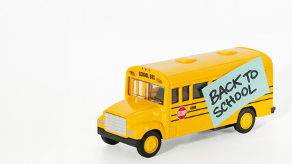 Yellow toy school bus with a 'BACK TO SCHOOL' sticky note on a white background. Perfect for educational themes, school promotions, and back-to-school campaigns. High-quality stock image.