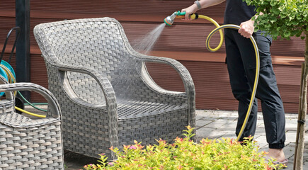 Anonymous cleaning, hose water washing wicker furniture from summer. Structures in backyard....