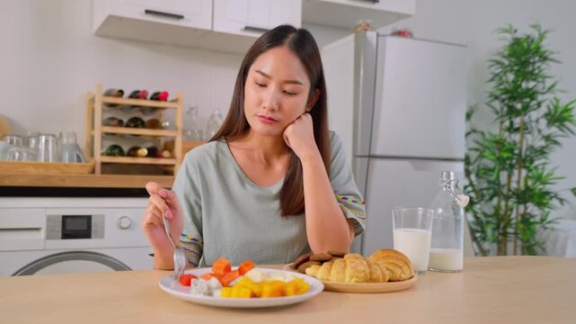 Asian unhappy woman on dieting, don't want to eat food in kitchen at home. 