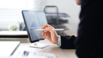 Fototapeta premium A businesswoman in a black suit is leaning over her desk, deeply focused on her work in a modern office environment