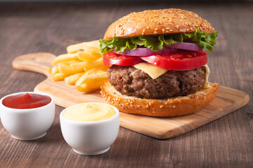 Homemade delicious hamburger with beef, onion, tomato, lettuce and cheese. Fresh burger close up on wooden rustic table with potato fries. Cheeseburger. Burger.