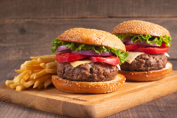 Homemade delicious hamburger with beef, onion, tomato, lettuce and cheese. Fresh burger close up on wooden rustic table with potato fries. Cheeseburger. Burger.