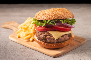 Homemade delicious hamburger with beef, onion, tomato, lettuce and cheese. Fresh burger close up on wooden rustic table with potato fries. Cheeseburger. Burger.