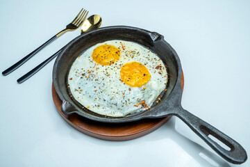 A plate of sunny side up eggs and a fork and knife on a white background