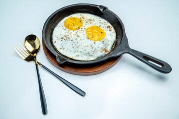 A plate of sunny side up eggs and a fork and knife on a white background