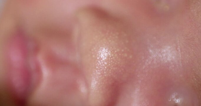 Close-up shot of the reddish skin of a sleeping newborn baby showing some white spots on its nose and its pinkish cute lips.