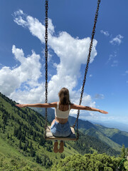 A 35-year-old girl in short denim shorts sits on a swing in the mountains. Kazakhstan, Almaty. Welcome to Kazakhstan! sporty lifestyle, heavenly swing, flying over the abyss