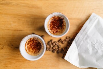 Top view of two cups of espresso coffee with coffee beans and a white bag on a wooden table.