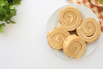 Coffee break roll cake in a white plate on white background, top view food table with free copy space
