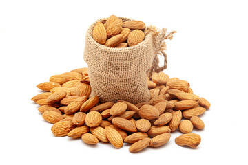 A jute bag filled with organic Almond kernels (Prunus dulcis) is placed over a pile of Almonds, isolated on a white background.