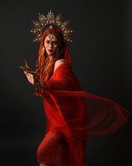 dramatic close up portrait a female model wearing a red silk dress and veil robes, with a ornate golden fantasy crown headdress. isolated on a dark studio background with  silhouette rim lighting 