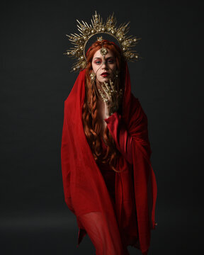 dramatic close up portrait a female model wearing a red silk dress and veil robes, with a ornate golden fantasy crown headdress. isolated on a dark studio background with  silhouette rim lighting 